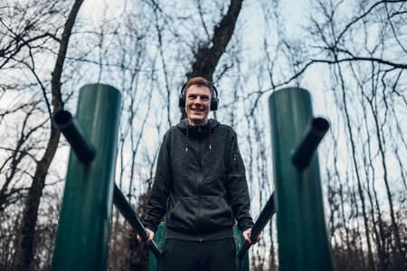 Redhead male doing fitness exercises and training in a forest. Listening music on a headphones while...