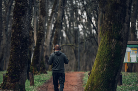 Rear view of a redhead male jogging and training for marathon on a forest road in amazing nature. Sport active concept. Runner using headphones and listening music during his training outside.の写真素材