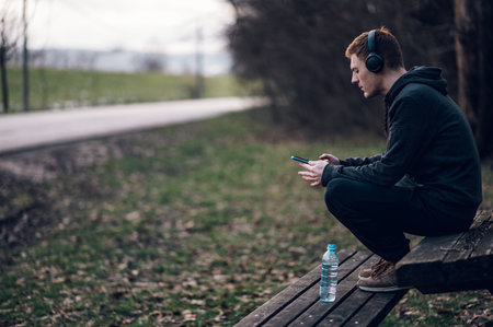 Athletic redhead young man using a smartphone while running outside in the forest. Listening music on a headphones while running. Athletic and healthy.の写真素材
