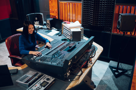 Middle aged woman music producer working on a mixing soundboard while in her sound studio. Recording...