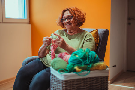 Senior woman knitting crochet slipper while relaxing at home in her armchair. Elderly leisure activities for good mental health concept. Art and craft concept.の写真素材