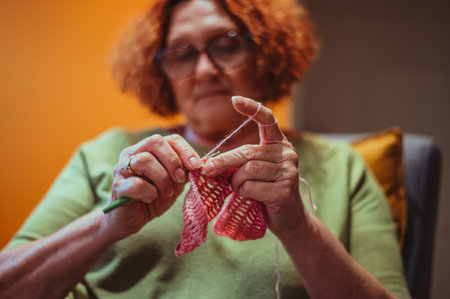 Senior woman knitting crochet slipper while relaxing at home in her armchair. Elderly leisure...