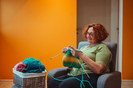 Mature woman holding knitting needles while making clothing accessories for her grandchildren at home. Handmade hobby stay home concept. Craft and DIY concept.の写真素材