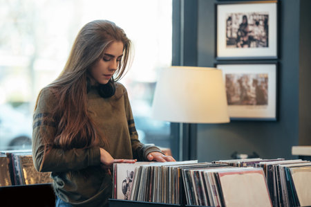 Young attractive woman choosing vinyl record in music record shop. Music addict concept. Old school...