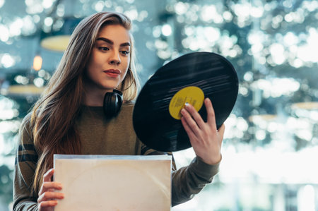 Beautiful woman holding a vinyl while selecting records in a shop. Young audiophile hipster woman in a record store. Vintage and retro style.の写真素材