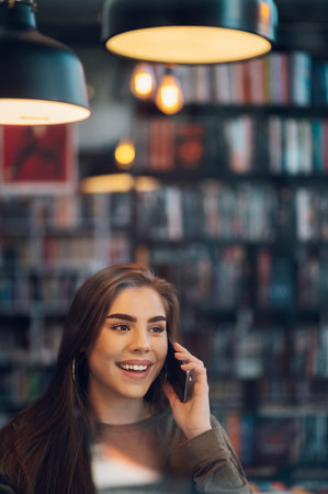 Young beautiful woman drinking coffee and looking at smartphone while sitting in a cafeteria....