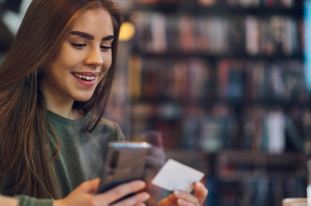 Young beautiful woman using smartphone and a credit card for online shopping while in a cafe during...