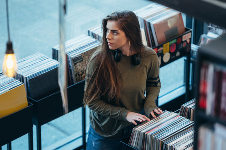 Beautiful young woman browsing records in the vinyl record store. Audiophile and music lover.の素材 [FY310196428064]