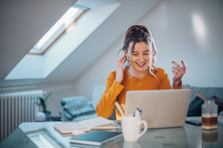 Happy businesswoman sitting and talking to colleagues in a meeting using her laptop computer while...