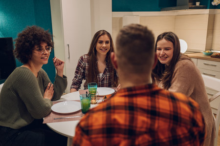 Group of friends gathered around a table in the kitchen are sharing a meal and having a good time together. Friends at dinner concept.の写真素材