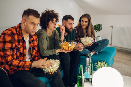 Cheerful group of friends enjoying a movie at home on the couch with snacks. Watching a comedy movie on a tv. Friends, home entertainment, free time concept.の写真素材