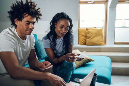 African american couple doing their accounts at home and using a laptop and a credit card for online...