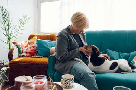 Happy young woman petting her gorgeous dog pet while sitting on the couch at home in the living room. Mixed breed. Staying at home activities.の写真素材
