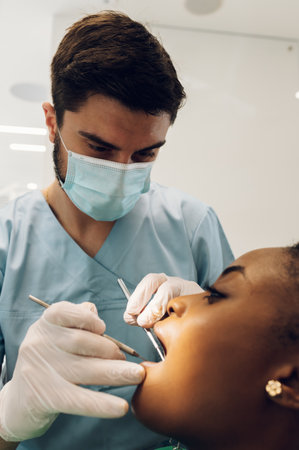 Competent stomatologist using sterile equipment while examining patient teeth. African american...