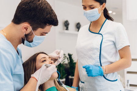 Male dentist with a help of his assistant fixing teeth of a woman patient in the dentists chair....