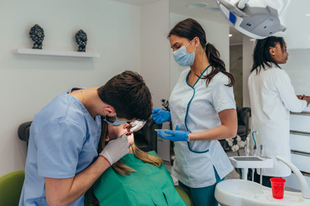 Young professional man doctor dentist working with a woman patient in dental clinic. Competent stomatologist using sterile equipment while fixing patient teeth.の写真素材