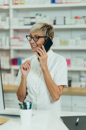Portrait of a beautiful senior female pharmacist working in a pharmacy and using smartphoneの写真素材