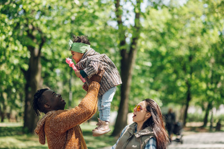 Happy diverse family of three spending their free time in the park and enjoying beautiful sunny day outside. Multiracial parents and their cute little daughter having fun together.の写真素材
