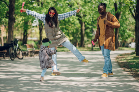 Happy diverse family of three spending their free time in the park and enjoying beautiful sunny day outside. Multiracial parents and their cute little daughter having fun together.の写真素材