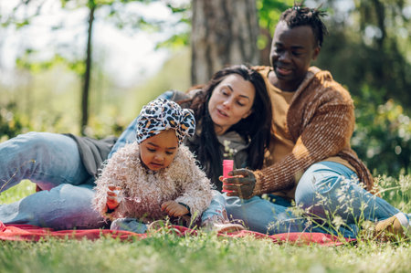 Lovely family of three spending time together in the park while blowing bubbles and bonding. Happiness and harmony in family life. Multiracial.の写真素材