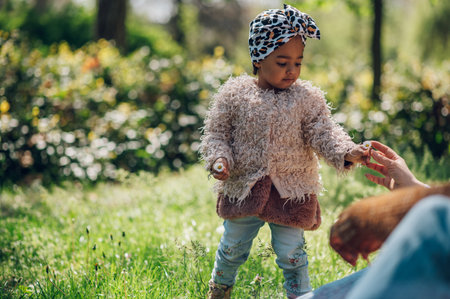Adorable black girl enjoys playing in a park or garden during a walk outside with her family. Funny african american toddler playing outdoor. Stylish and fashionable.の写真素材
