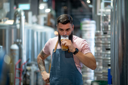 Handsome man examining the quality of craft beer at brewery. Male brewer working at beer factory checking the beer quality. Testing beer at a modern brewery.の写真素材