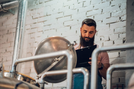 Bearded caucasian man with clipboard taking notes while working at craft brewery. Manufacture, business and people concept.の写真素材