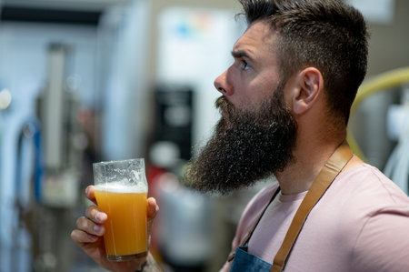 Portrait of a bearded man working in a brewery and checking quality of the craft beer. Brewery owner tasting beer from the best bach.の写真素材
