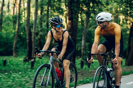Caucasian fit couple practicing in cycling wearing sports equipment while riding a bike outside. Concept of healthy lifestyle, sport, action, motion. Looking at each other. Copy space.の写真素材