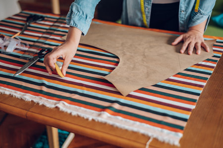 Concentrated middle aged woman tailor using pattern dress detail for sewing machine and a chalk...