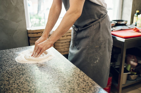 Male worker in a pizza place preparing dough for pizza on counter top. Man hands working with dough...