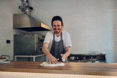 Male worker in a pizza place preparing dough for pizza on counter top. Man hands working with dough and flour. Pizzeria. Focus on a pizza master chef working in a kitchen.の写真素材