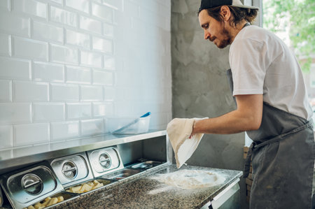 Kitchen chef kneading dough for pizza on a counter while working in a pizza place. Worker in a pizzeria stretches raw pizza dough.の写真素材