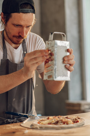 Hands of a kitchen chef making pizza and placing components on top while working in a pizza place. Arranging raw ingredients on the dough before baking. Grating cheese with grater.の写真素材