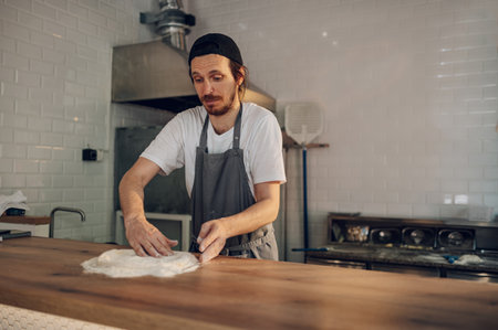 Skilled chef preparing dough for pizza rolling with hands while working in a pizza place. The process of making pizza. Working on a wooden counter.の写真素材