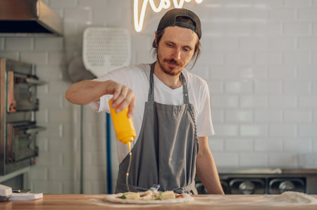Man pizza master prepares pizza according to customer requests. Process of placing ingredients on a pizza. Pizza place and tasty food concept.の写真素材
