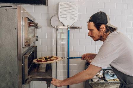 Close-up portrait a cheerful chef working in a pizza place and putting the pizza into the owen. Smiling chef wearing apron uniform and posing.の写真素材