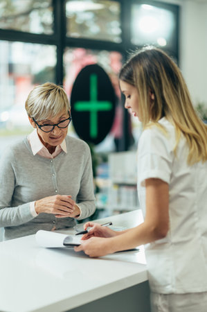 Happy senior woman customer buying medications at drugstore while talking with a female pharmacistの写真素材