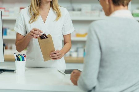 Female pharmacist selling medications at drugstore to a senior woman customer and packing them in a paper bagの写真素材