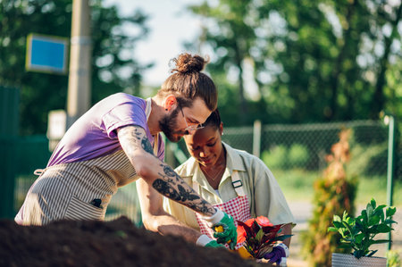Couple of smiling multiracial gardeners wearing apron transplanting pot plants while working in a greenhouse. Professional florist taking care of the flowers and working in a plant nursery.の写真素材