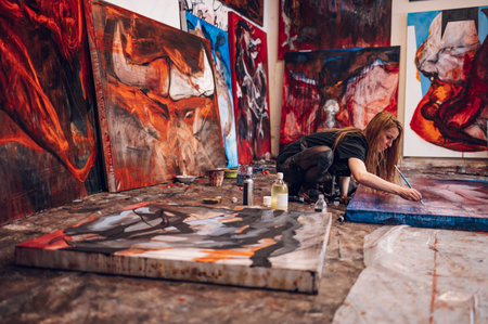 Indoor shot of a professional female artist painting on big canvas in a creative studio. Young talented woman artist working on her painting with oil pant while using hands. Artist studio interior.の写真素材