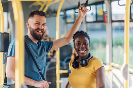 Young multiracial couple of friends chatting on a bus together. Two best friends are talking while standing in a bus. People in a public transport concept. Diverse romantic couple riding in a vehicleの写真素材