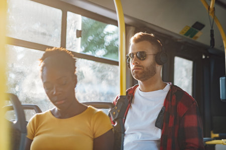 Handsome man commuting to work by bus and listening music on a headphones. Bearded hipster guy enjoying his favorite song during a bus ride. People travel transport concept.の写真素材