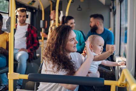 Mother holding her child while sitting next to her in the bus. Mom holding her infant baby boy while riding in a public transportation. Cute toddler boy looking out the window while his mom holds himの写真素材