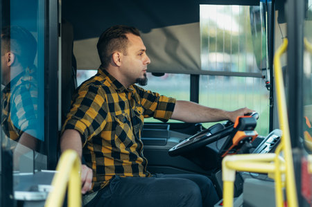 Professional bearded caucasian bus driver at steering wheel. Young professional driver wearing a checkered shirt driving tour bus. Traveling and Tourism Concept.の写真素材