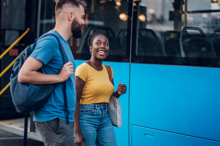 Multiracial friends standing at a bus stop and waiting for public transport at sunny day. Diverse passengers waiting for a bus. Focus on a smiling african woman. Copy space.の写真素材