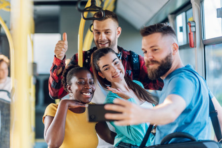 Smiling group of diverse friends riding together on a bus and taking selfie with a smartphone. Multiracial group of people enjoying travel or ride on public vehicle and having fun.の写真素材