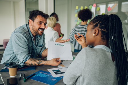 Two diverse businesspeople chatting in an office. Excited african american female sharing ideas or startup business plan with caucasian male coworker. Work break concept. Multiracial team.の写真素材