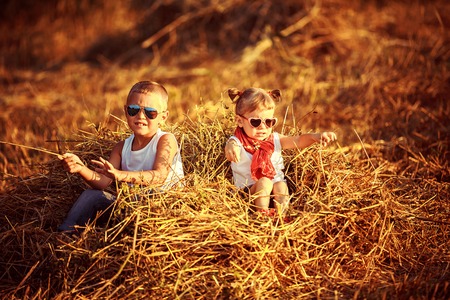 Summer landscape with hay cocks, couple children, brother and sister sitting on large pile of hayの写真素材