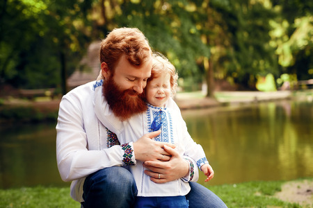 Red-heared father and red-heared son having fun in a park in a traditional white shirts with ornamentの写真素材